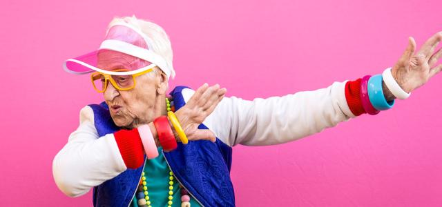 An elderly woman wearing brightly colored, hip clothing doing a funny pose.